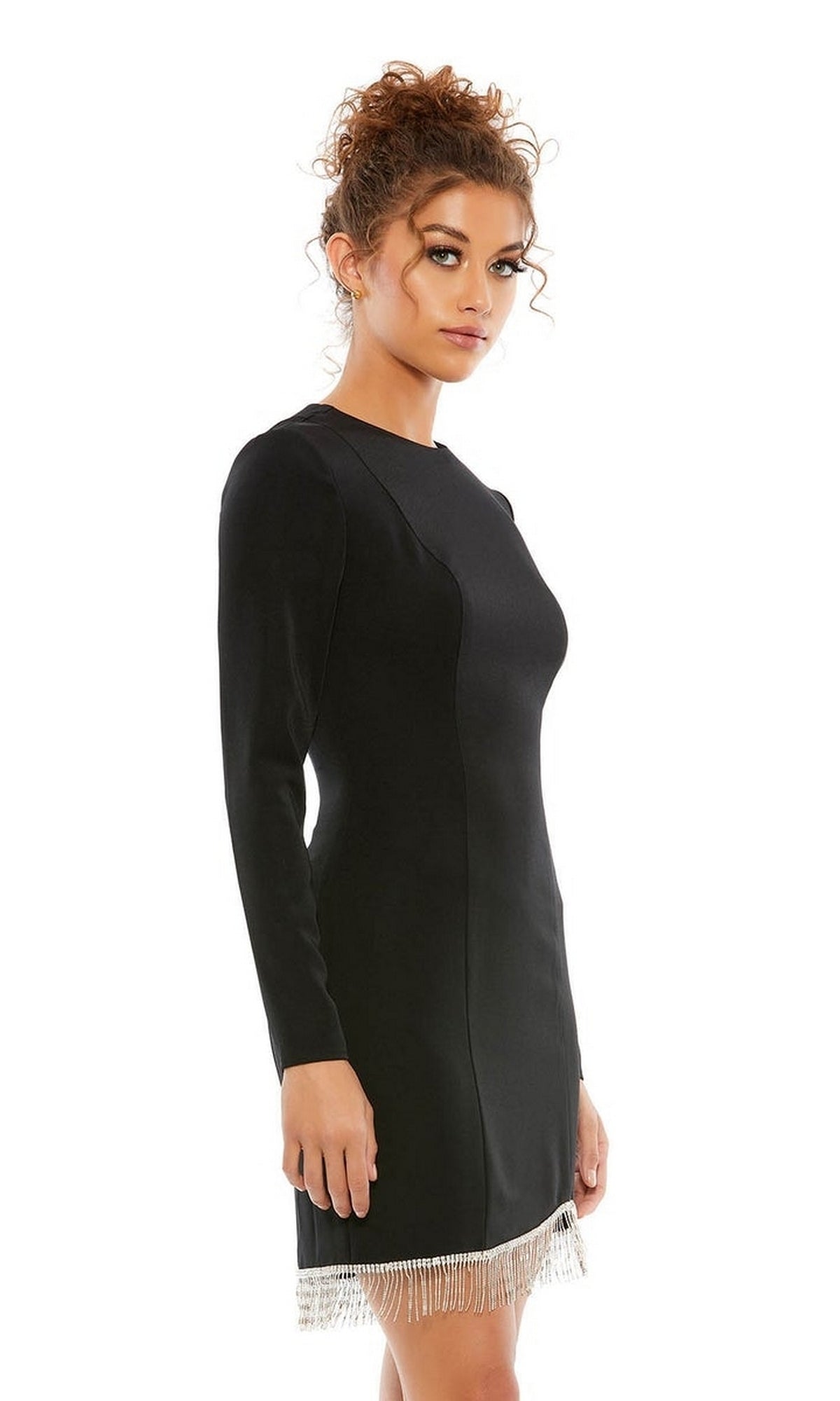 A woman poses elegantly in the Mac Duggal Short Homecoming Dress 26679—a black fitted dress with long sleeves and a beaded fringe hem—against a plain white background.